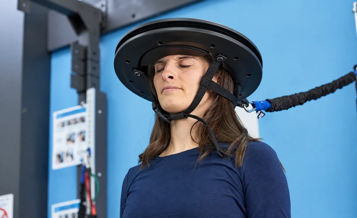 Clinic employee demonstrating Iron Neck headgear with its resistance tether attached