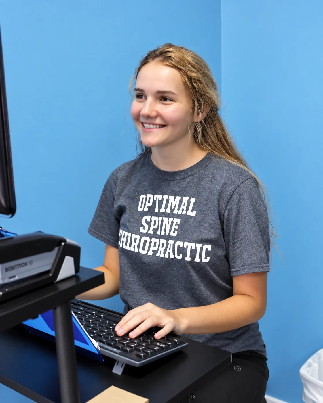 A clinic team member at the workstation in an Optimal Spine shirt